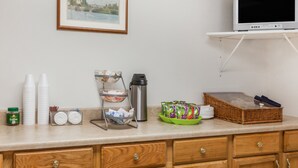 A kitchenette with a coffee station, a TV on a shelf, and a framed painting on the wall. - Travelodge by Wyndham Elkton University Area (Elkton)
