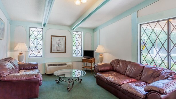 A living room with two leather sofas, a glass coffee table, a television, and a fireplace. - Travelodge by Wyndham Elkton University Area (Elkton)