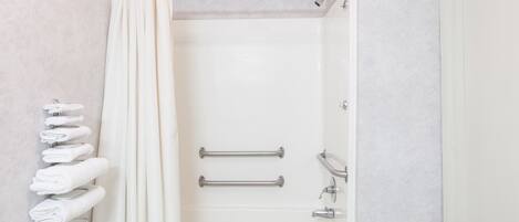 A bathroom with a bathtub, two grab bars, and a towel rack with towels.