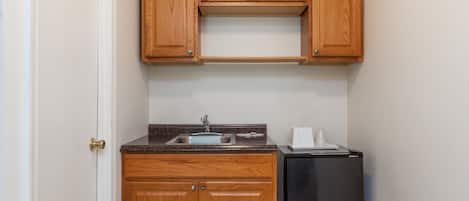 A compact kitchen with wooden cabinets, a stainless steel refrigerator, and a sink.