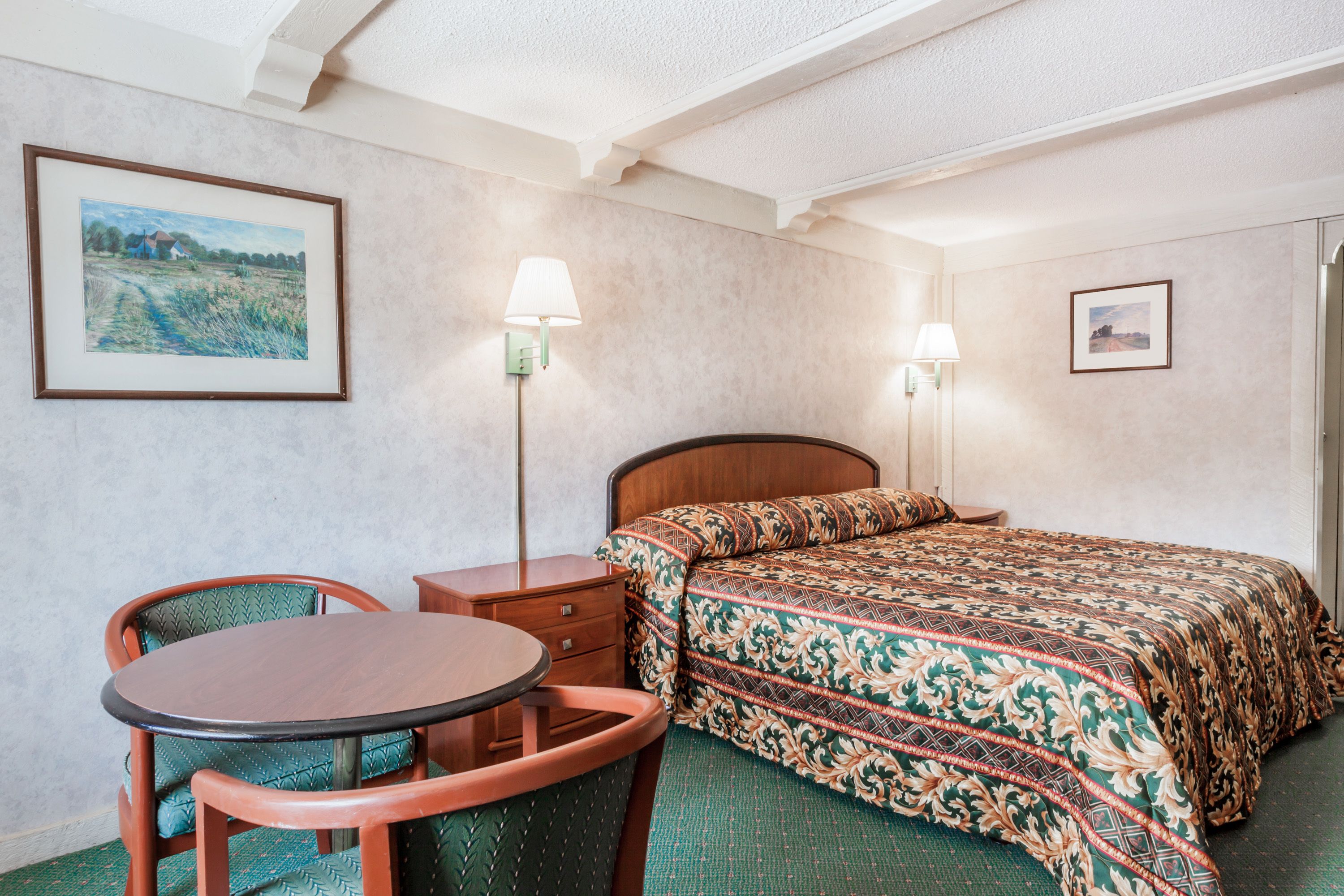 A hotel room with a bed, a desk, a chair, and two wall-mounted lamps.
