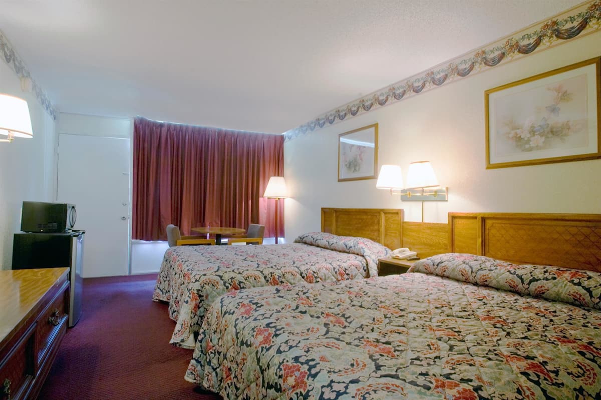 A hotel room with two beds, a desk with a chair, a TV, and a lamp.