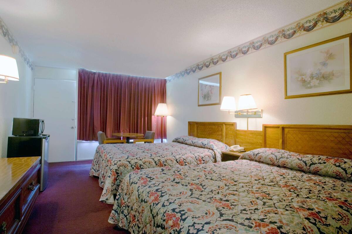 A hotel room with two beds, a desk with a lamp, a chair, a television, and a door.