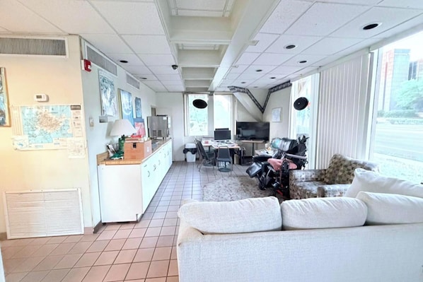 A compact hotel room with a kitchenette, a dining area, a sofa, and large windows.