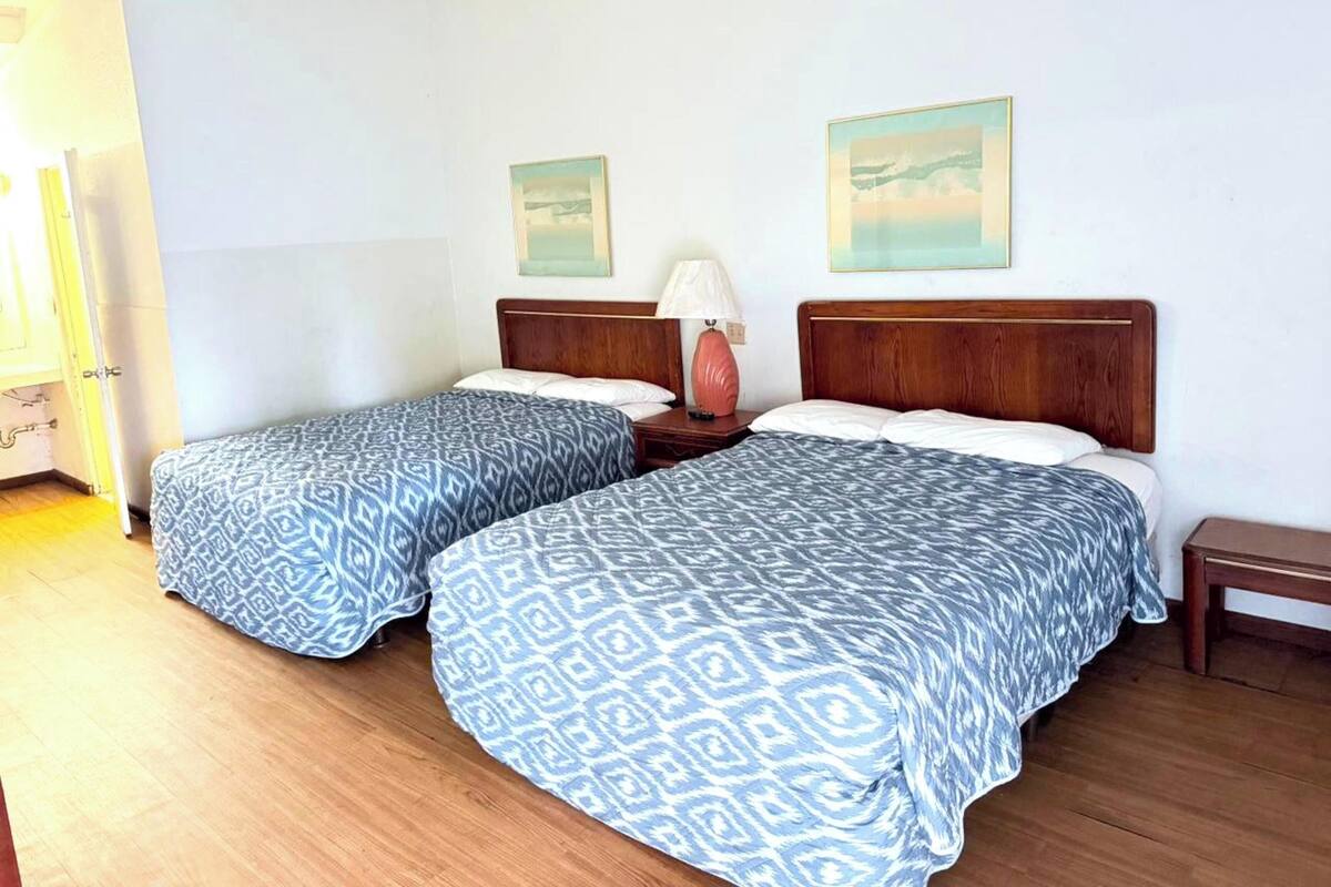 A room with two beds, a nightstand, a lamp, and two wall-mounted pictures.