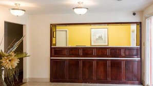 A reception area with a glass table, a red carpet with a logo, wooden paneling, and a yellow wall with a framed picture. - Econo Lodge Petersburg - Fort Lee (Petersburg)