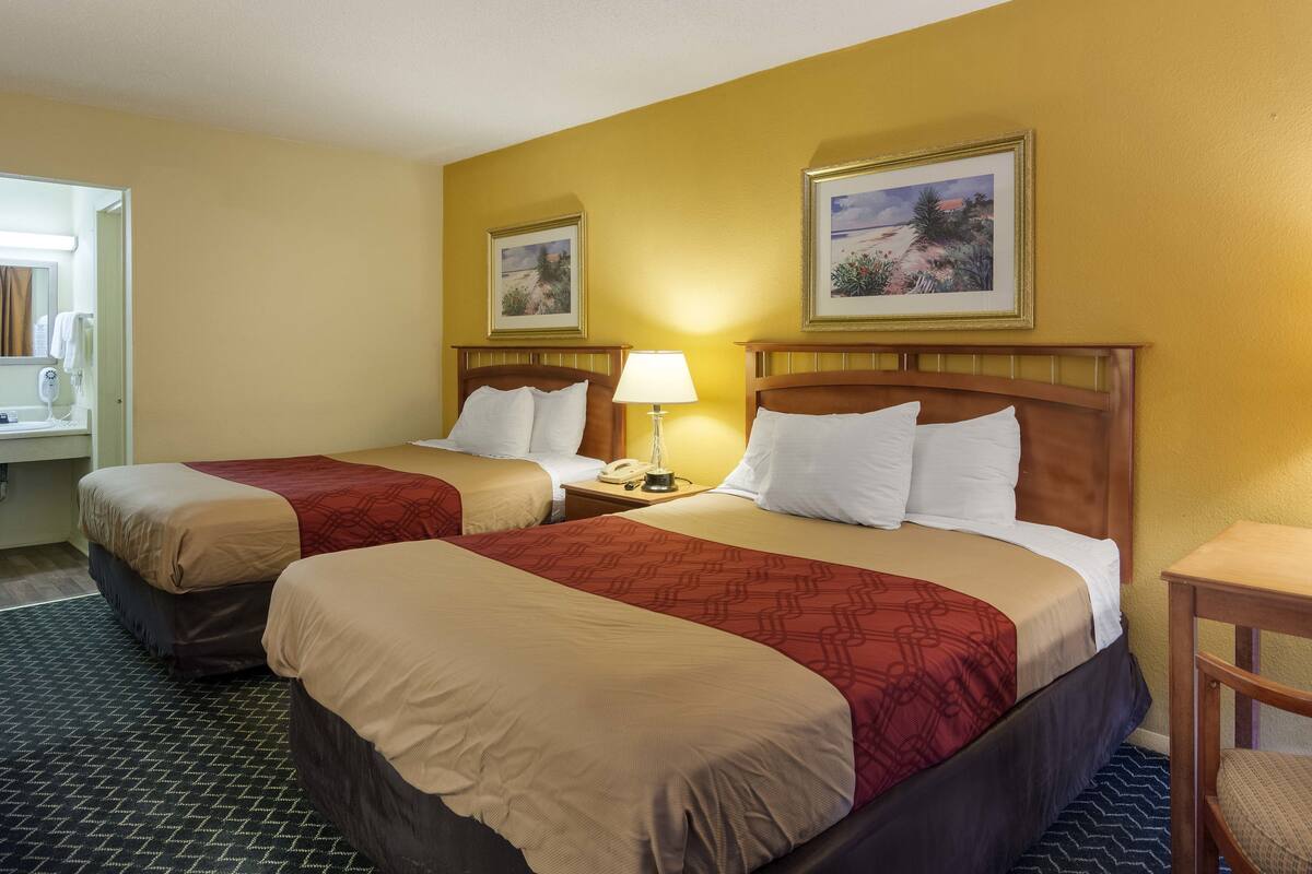 Una camera d'albergo con due letti, un comodino con una lampada, un telefono e un quadro appeso al muro.