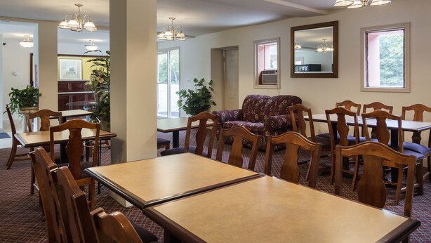 A dining area with wooden tables and chairs, a floral sofa, and pendant lighting. - Econo Lodge Petersburg - Fort Lee (Petersburg)