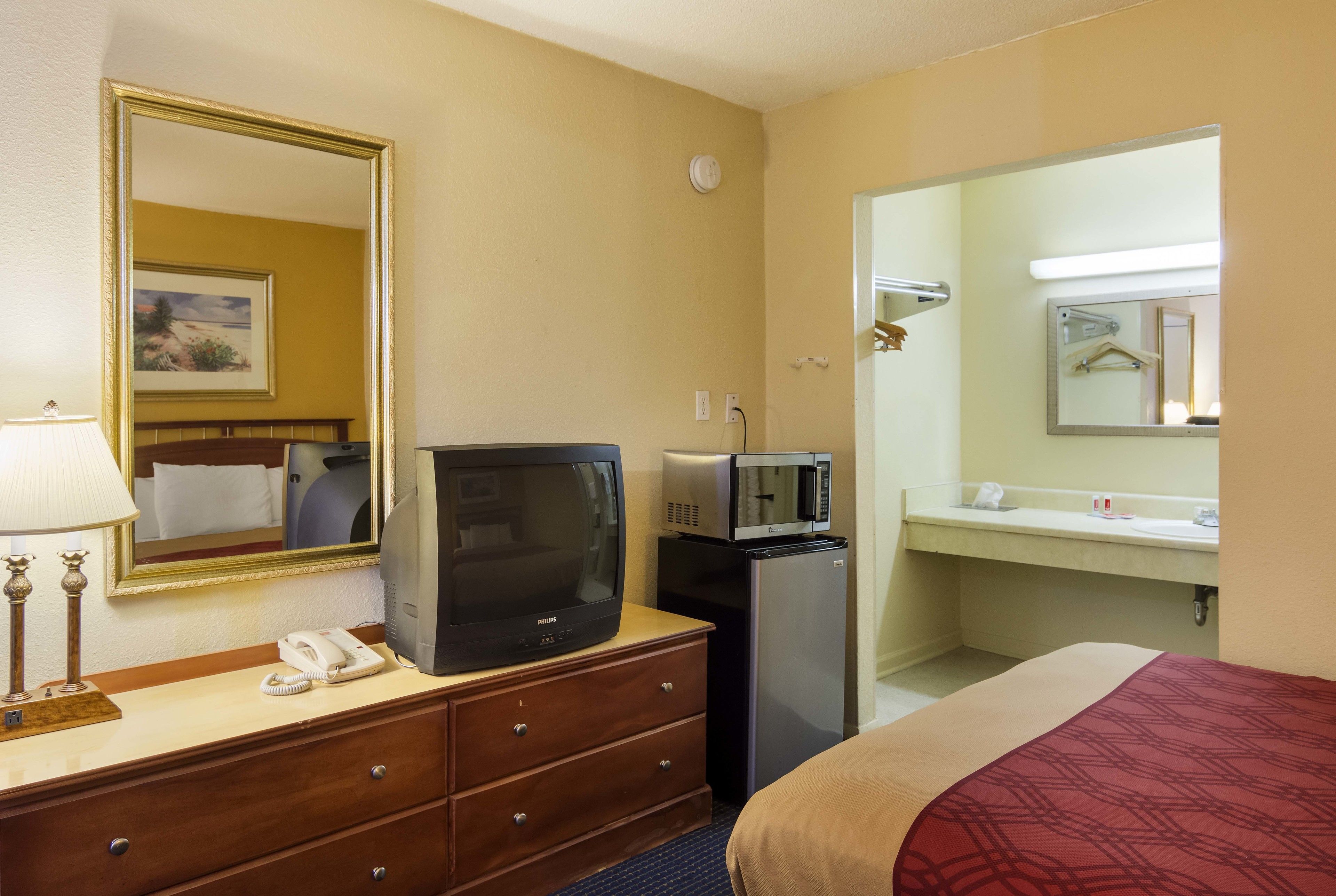 A hotel room with a bed, a dresser with a television, a microwave, a telephone, and a mirror.