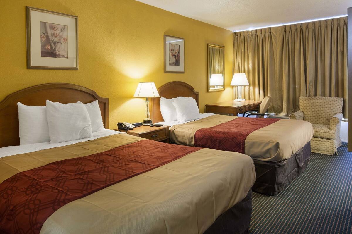 Camera d'albergo con due letti, una sedia, una scrivania e una lampada.