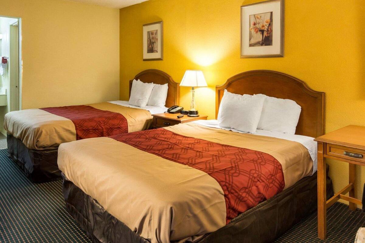 Una camera d'albergo con due letti, ciascuno con una testata in legno, un comodino con una lampada e un quadro appeso al muro.