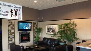 A lobby with leather sofas, a fireplace, a television, and a sign advertising the Chamber of Commerce. - King's Inn (Belle Fourche)
