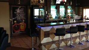 A bar area with a counter, stools, and a television screen. - King's Inn (Belle Fourche)