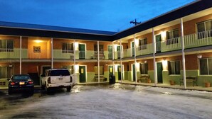 A multi-story motel with a central courtyard, featuring a white SUV and a black car parked in the driveway. - King's Inn (Belle Fourche)