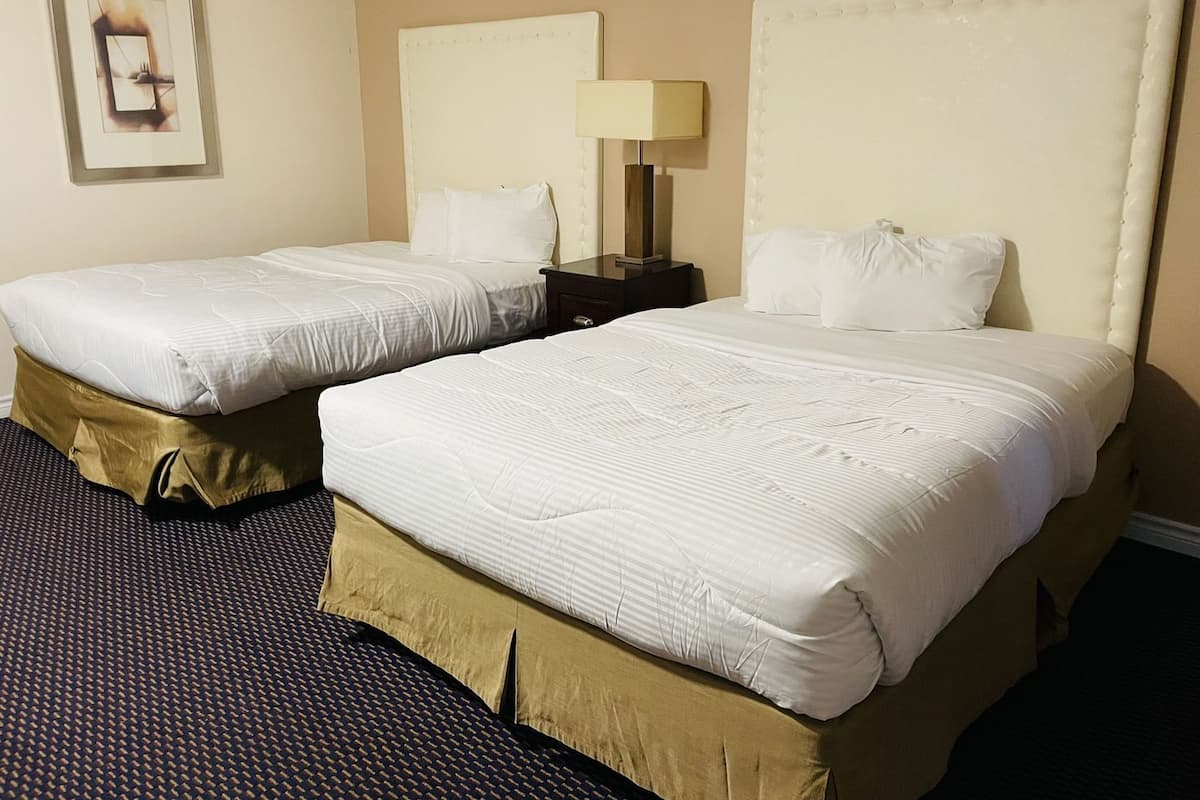 A hotel room with two beds, a nightstand with a lamp, and a framed picture on the wall.
