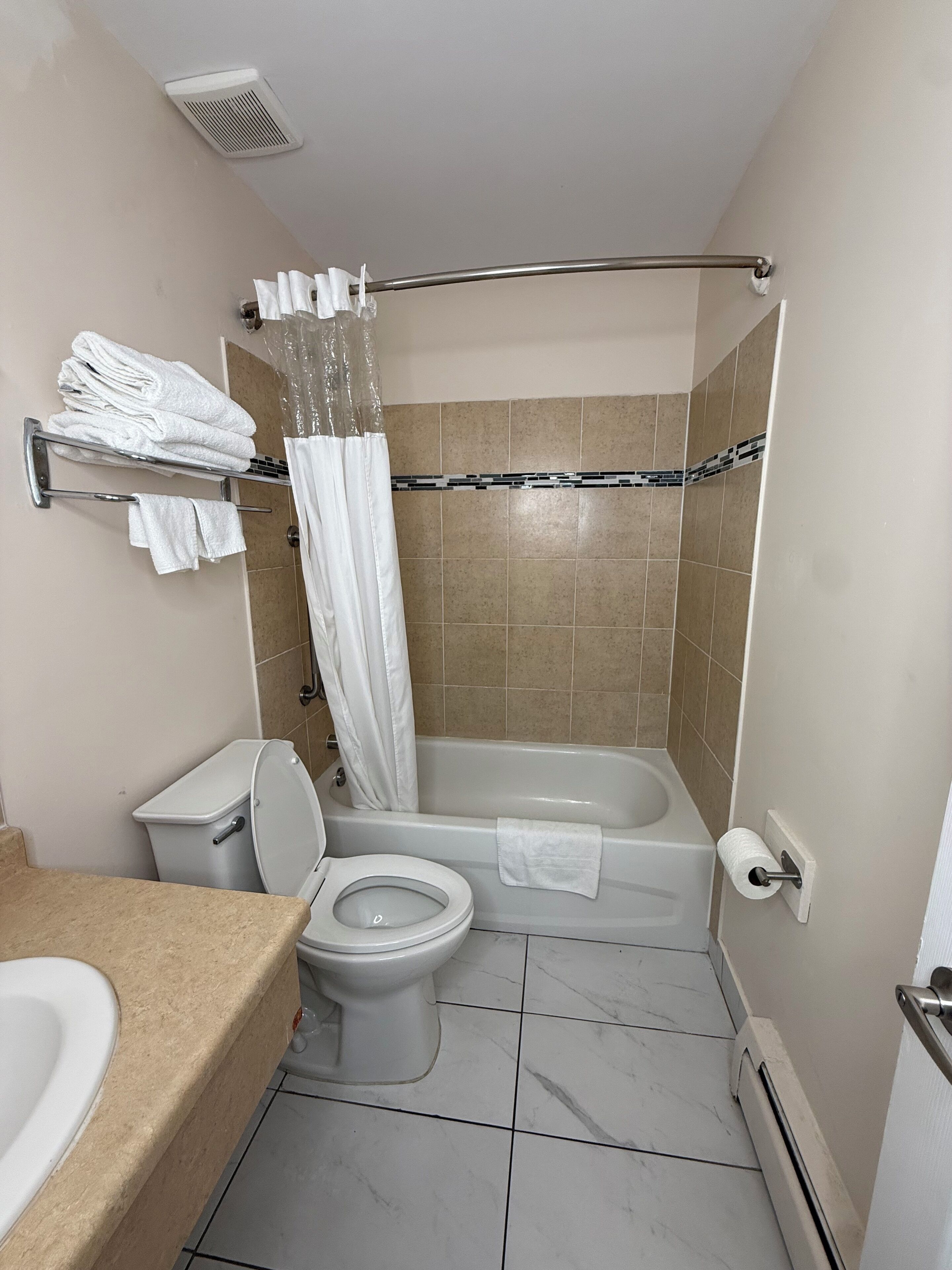 Un baño con inodoro, bañera, cortina de ducha, toallero y dispensador de papel higiénico.
