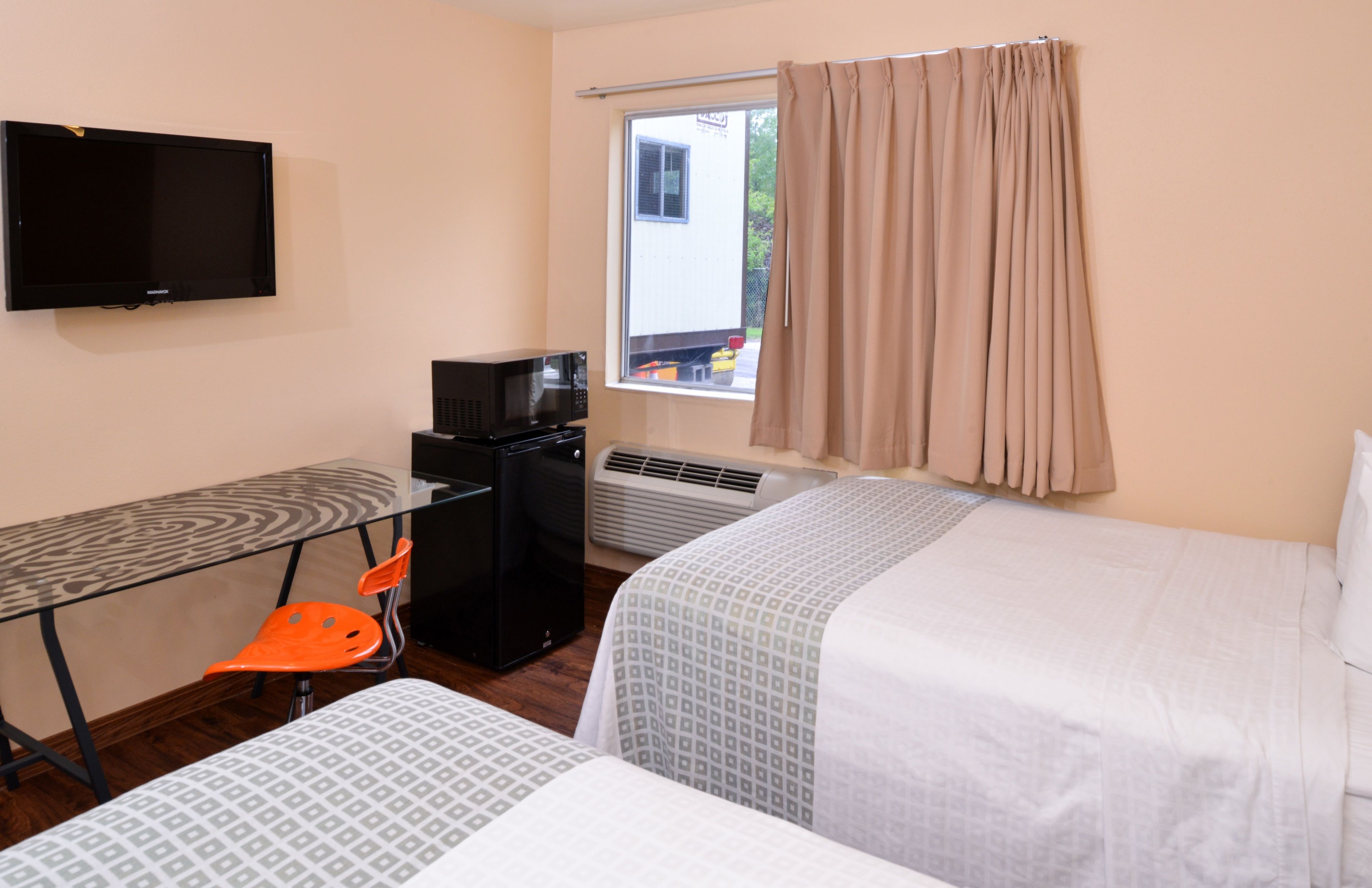 Une chambre d’hôtel comprenant un lit, un bureau avec une chaise, une télévision et une fenêtre avec des rideaux.