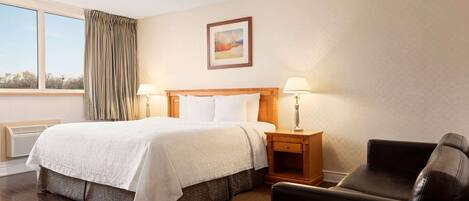 A hotel room with a large bed, two bedside lamps, a chair, a window with curtains, and a painting on the wall.