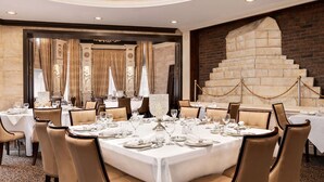 A formal dining room with round tables, beige chairs, and white tablecloths.