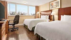 A hotel room with two beds, a desk with a chair, a television, and a window with curtains.