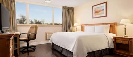 A hotel room with a bed, a desk, a chair, a television, and a window with curtains.