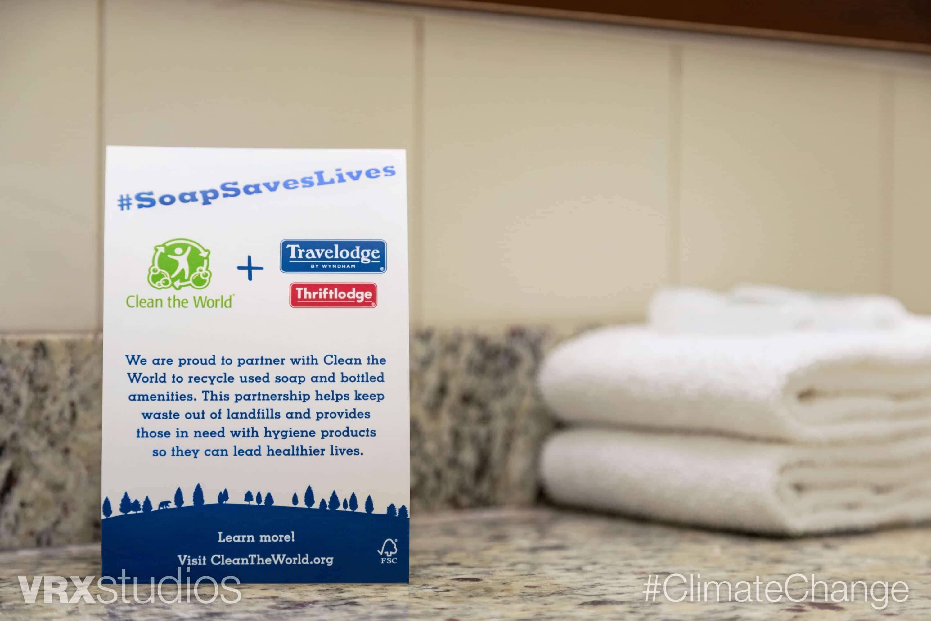 A bathroom with a sign promoting #SoapSavesLives, Clean the World, and TraveLodge by Wyndham.