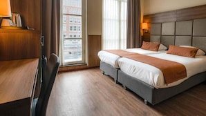 A hotel room with a bed, bedside table, lamp, and a view of buildings through the window. - OZO Hotels Cordial Amsterdam (Amsterdam)