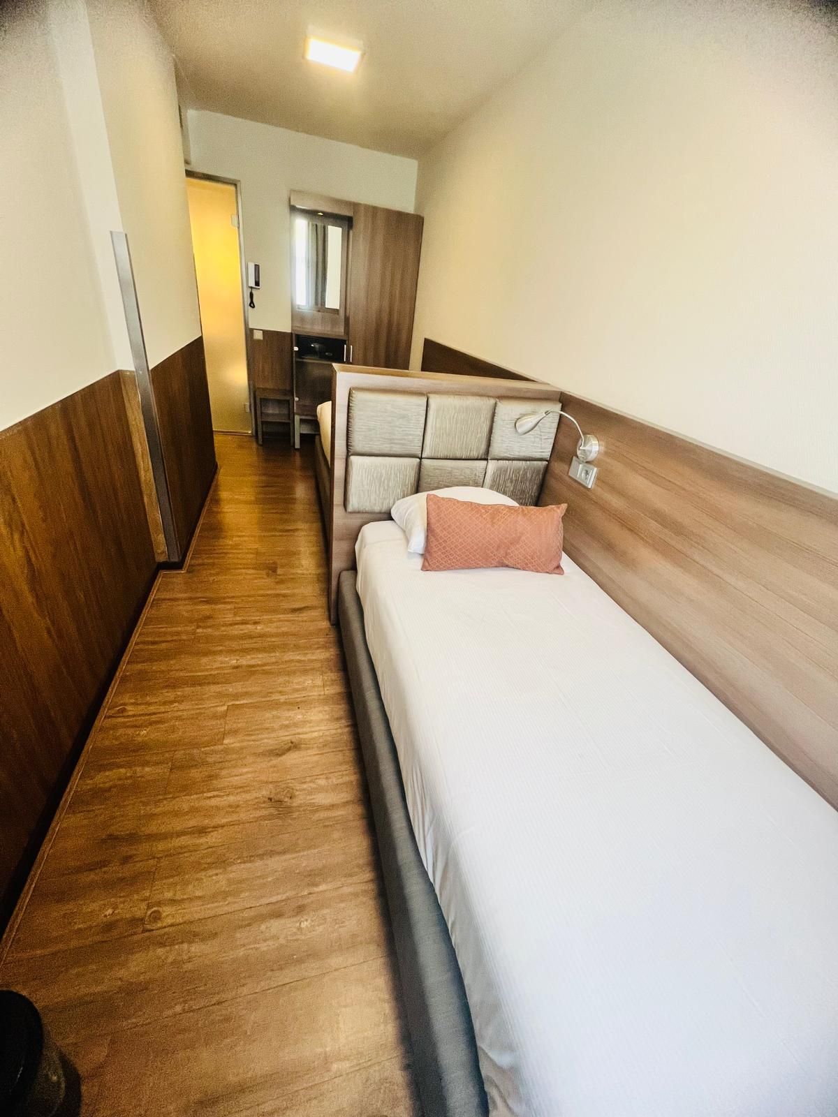Un pasillo estrecho con piso de madera que conduce a una habitación con una cama y un escritorio pequeño.