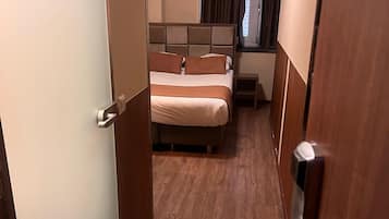 A narrow hallway leading to a bedroom with a bed, a bedside table, and a window with curtains.