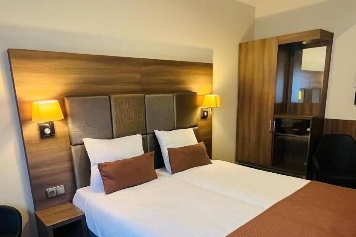 Habitación de hotel con una cama grande, dos mesitas de noche, un buró y un armario.