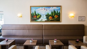 A modern interior with a large brown sofa, two small tables with vases, and a wall-mounted painting of a mountain landscape. - OZO Hotels Cordial Amsterdam (Amsterdam)