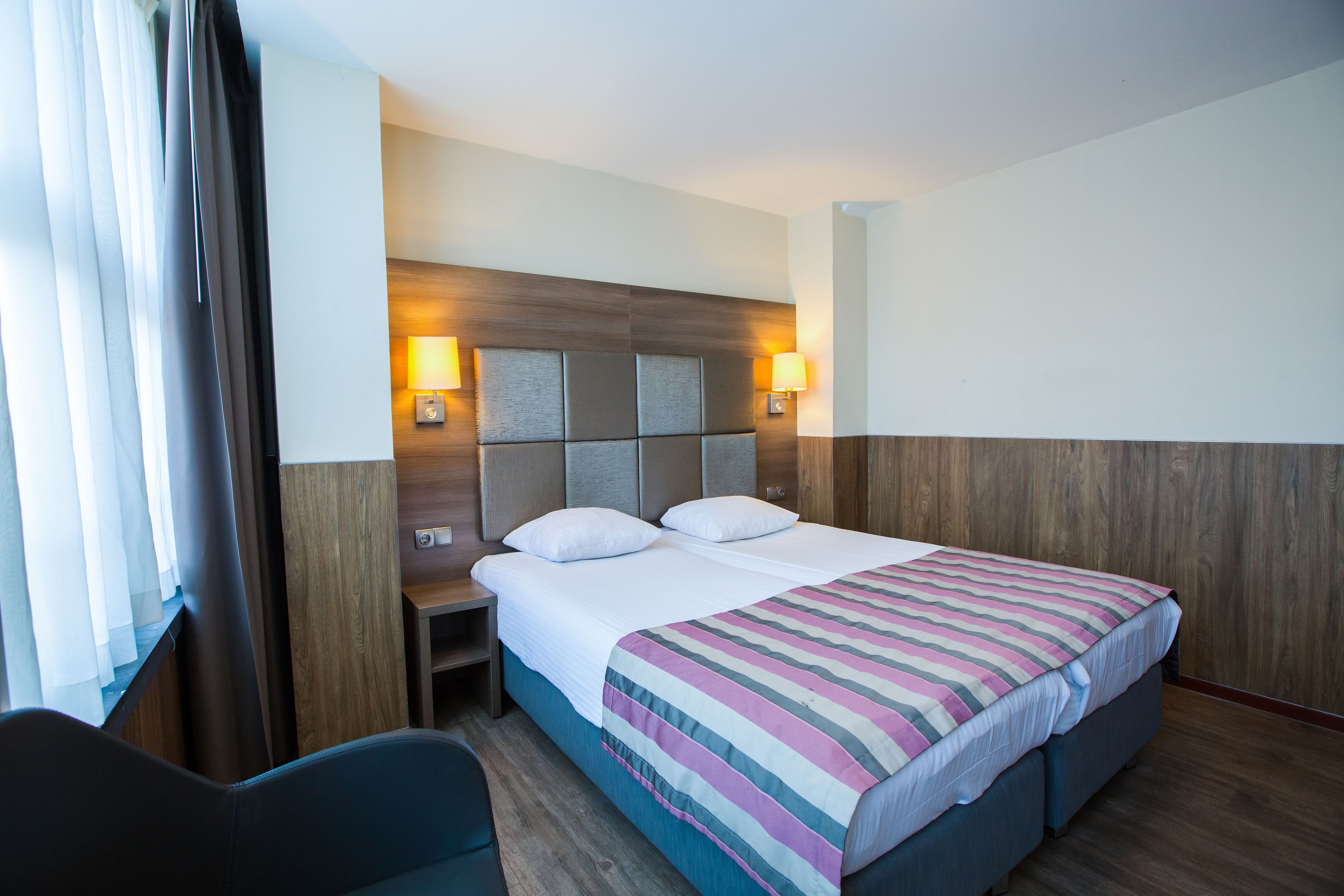 A hotel room with a large bed, a nightstand, a chair, and a wooden headboard.