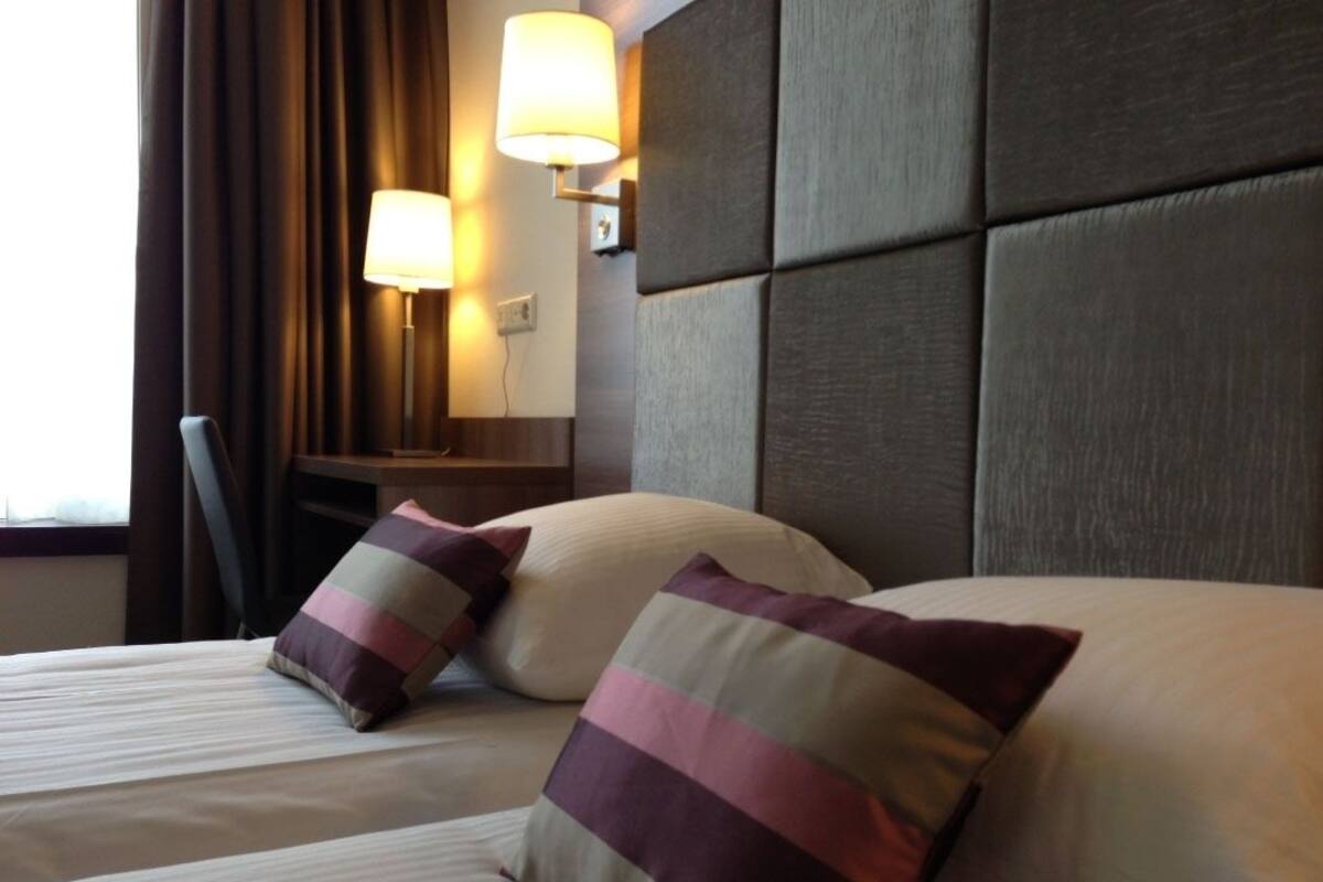 Habitación de hotel con una cama grande, dos almohadas, una mesita de noche y una lámpara de pared.