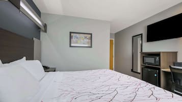 A hotel room with a bed, a desk with a computer, a microwave, and a small refrigerator.