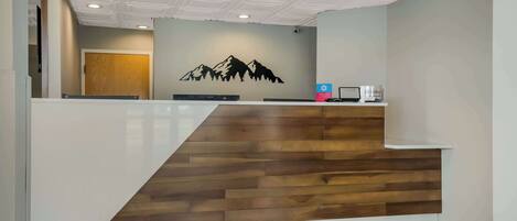 A reception area with a wooden reception desk, a wall-mounted computer, and a door in the background.