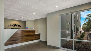 A reception area with a wooden reception desk, a mountain mural, and a large sliding glass door leading to a landscaped outdoor area. - SureStay Plus Hotel by Best Western Sevierville (Sevierville)