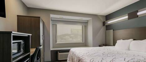 Una habitación de hotel compacta con una cama, un escritorio integrado con microondas, un calefactor y una ventana con vistas a edificios.