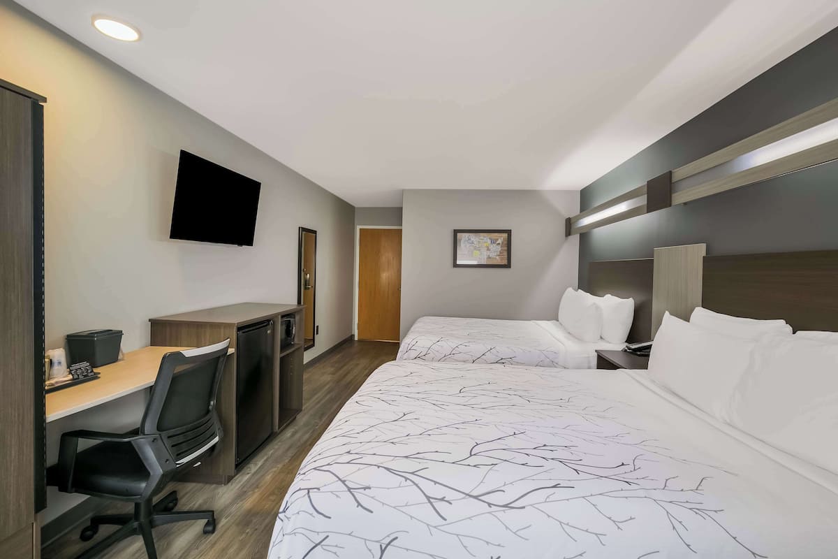 A hotel room with a bed, a desk with a chair, a television, and a door.
