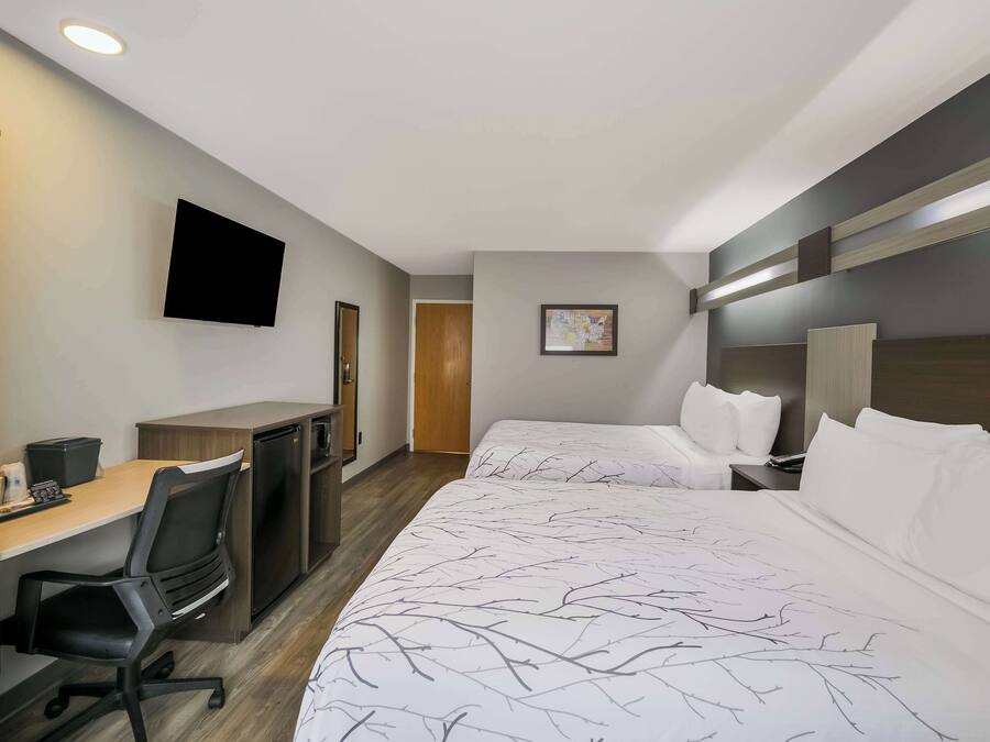Quarto de hotel com cama, escrivaninha com cadeira, televisão e porta.