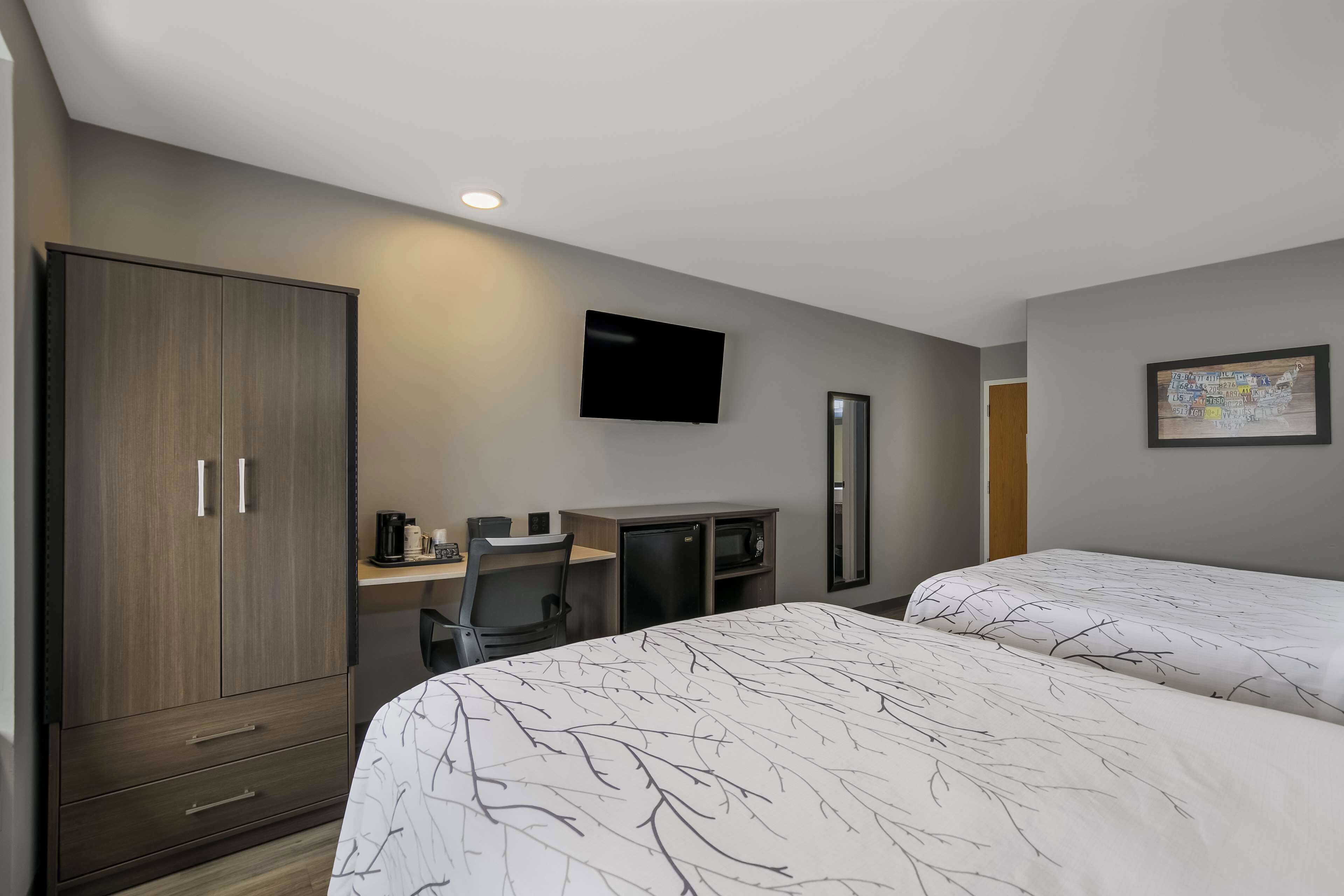 Habitación de hotel con dos camas, un escritorio con silla, televisión, armario y un refrigerador pequeño.