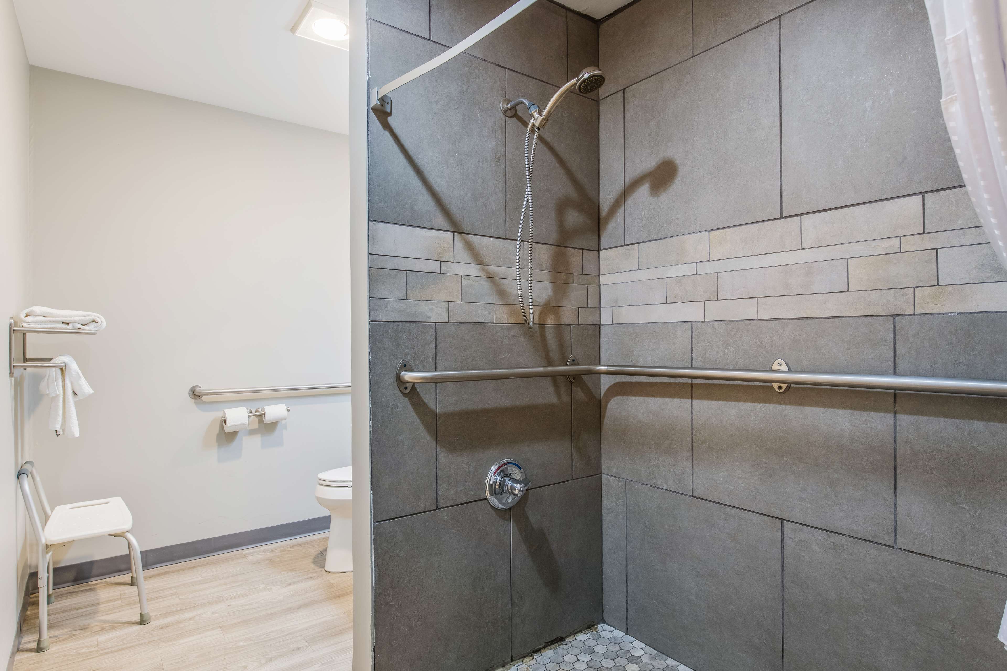 Un baño moderno con ducha, barras de apoyo, inodoro y asiento accesible para silla de ruedas.
