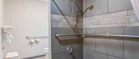 Un baño moderno con ducha, barras de apoyo, inodoro y asiento accesible para silla de ruedas.