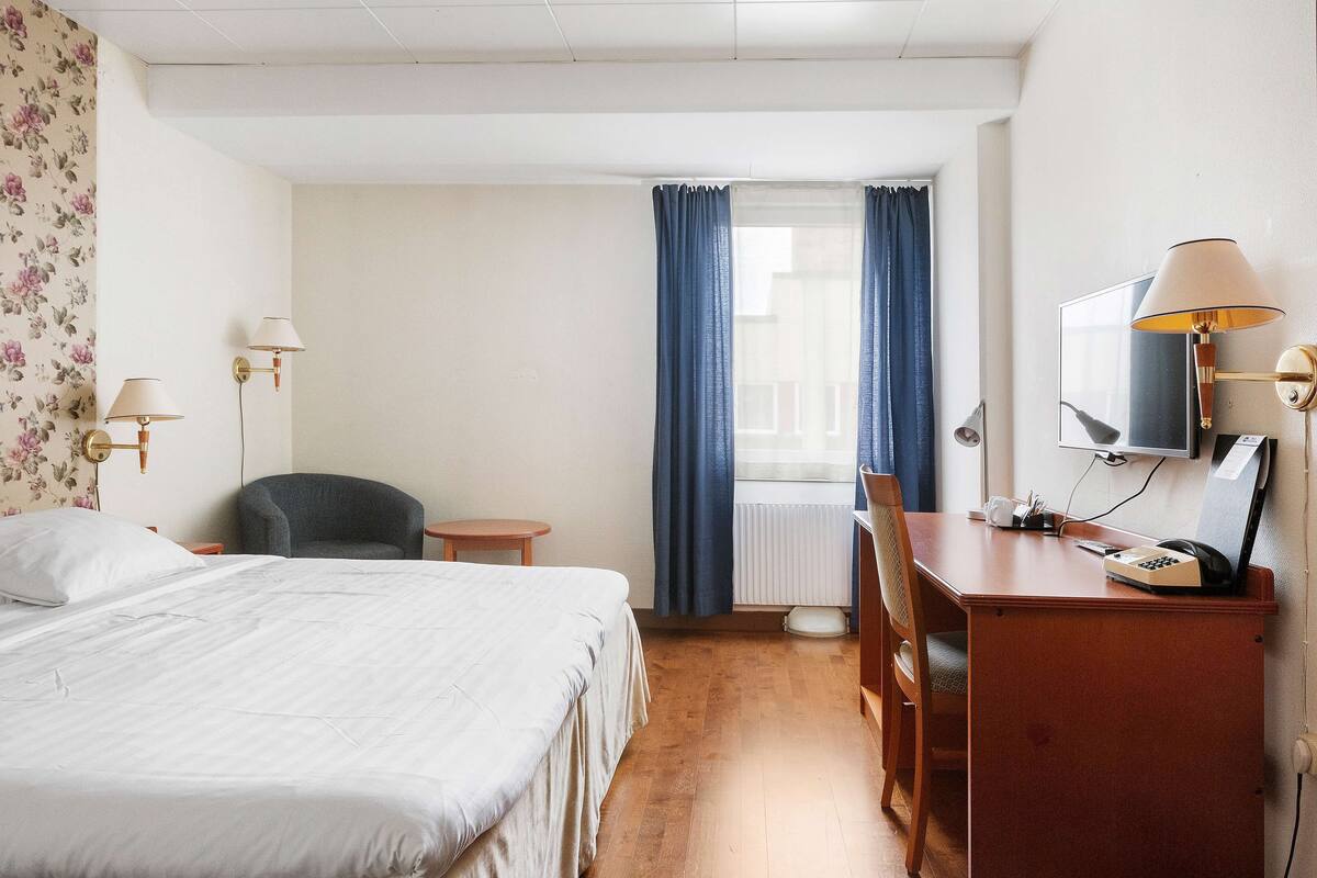 A hotel room with a bed, a desk, a chair, a television, and a window with curtains.