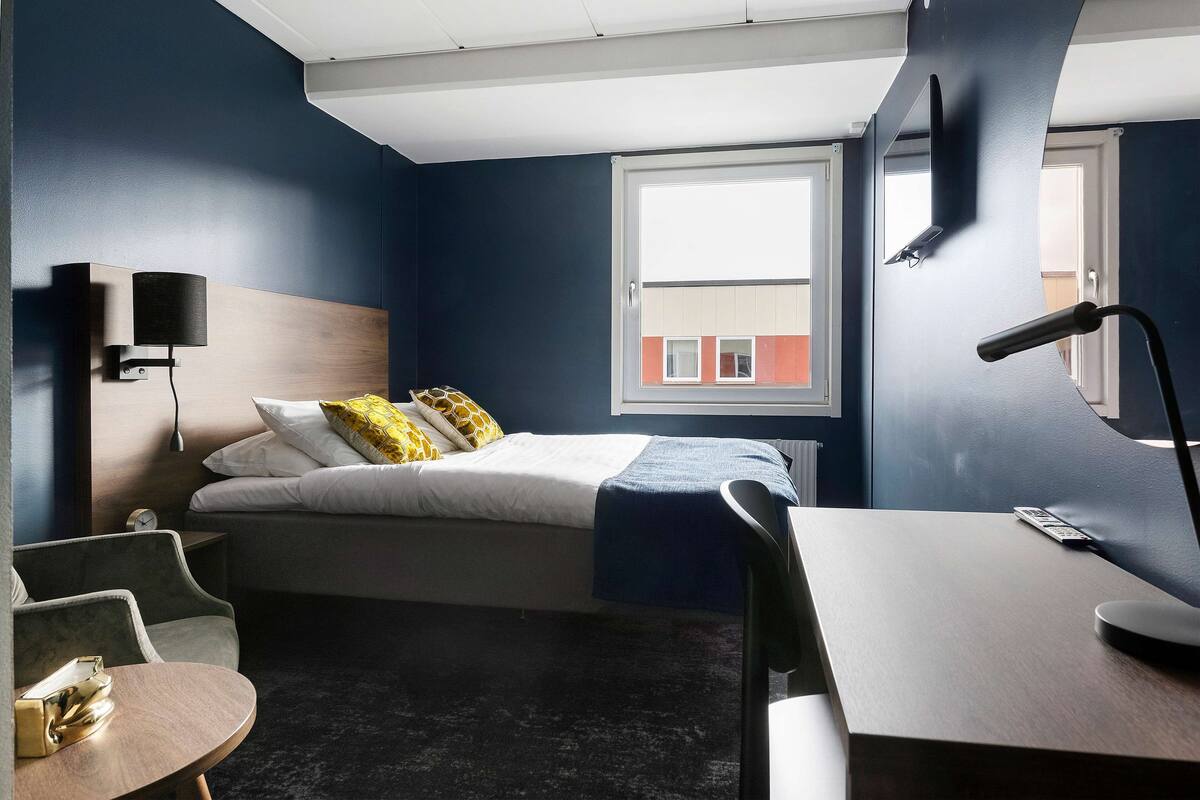 A modern hotel room with a bed, desk, and seating area.