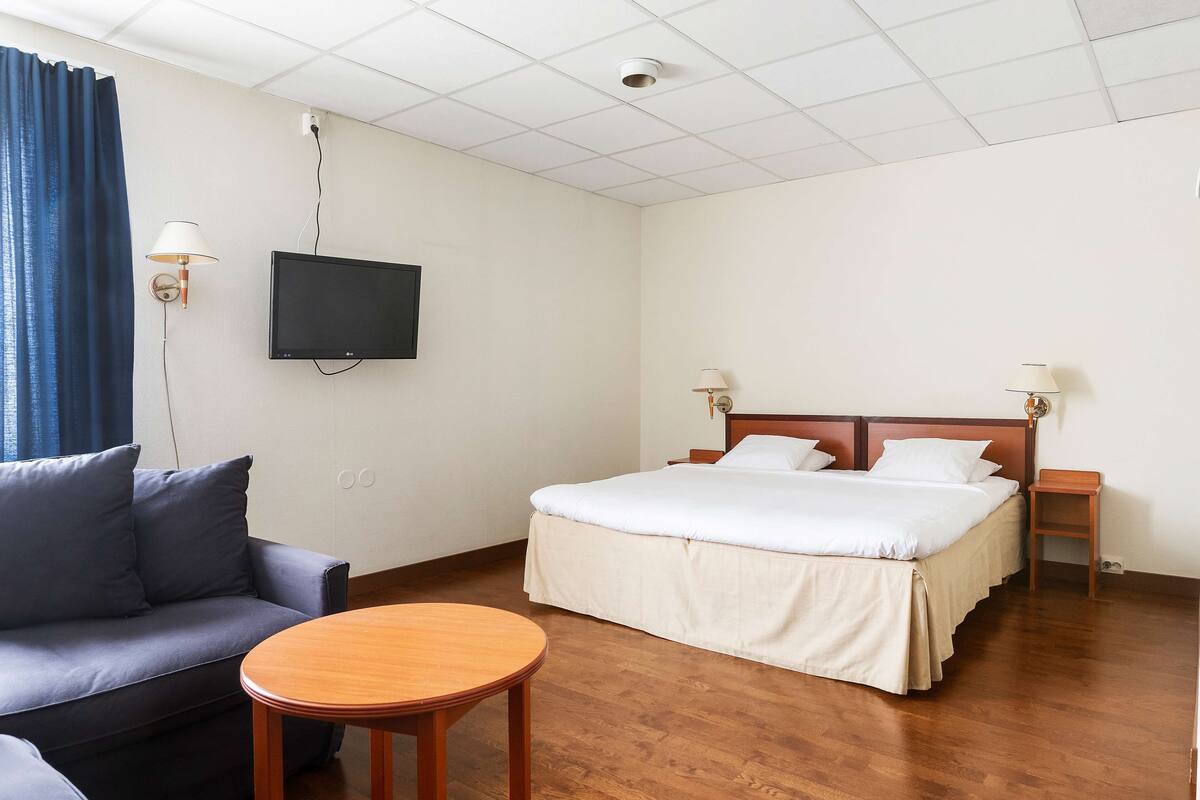 A hotel room with a bed, a sofa, a TV mounted on the wall, and a small wooden table.