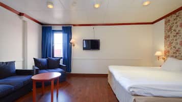 A hotel room with a sofa, a small table, a bed, a TV, and a window with curtains.