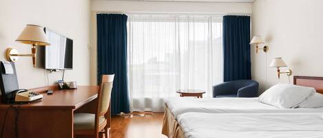 Una habitación de hotel con escritorio, silla, dos camas, televisor y ventana con cortinas.