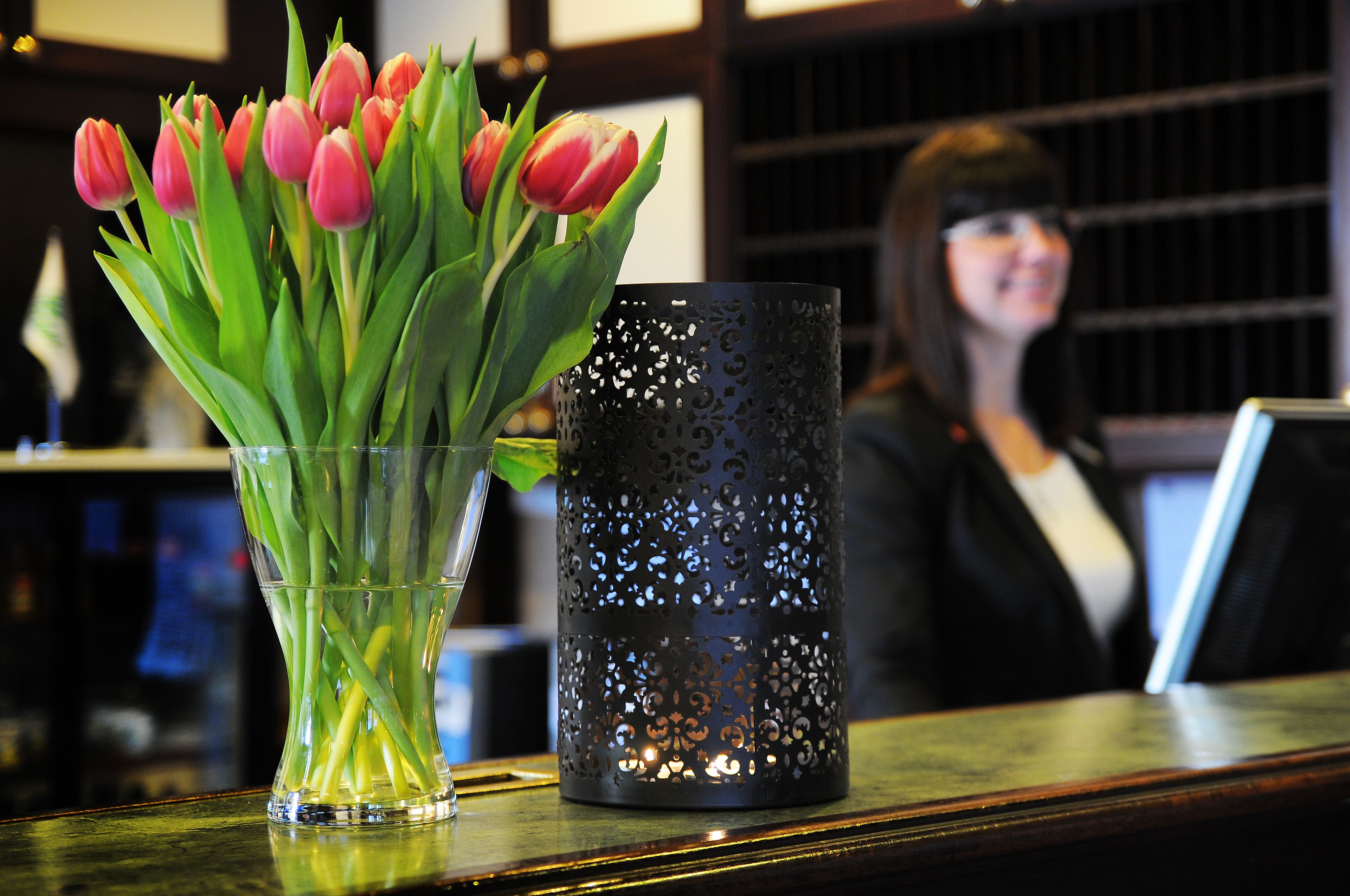 Un florero de vidrio transparente con tulipanes rosados y un candelabro decorativo negro sobre una barra.