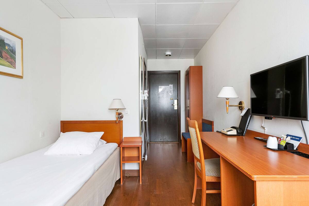 A hotel room with a bed, a desk, a chair, a TV, and a door leading to another room.