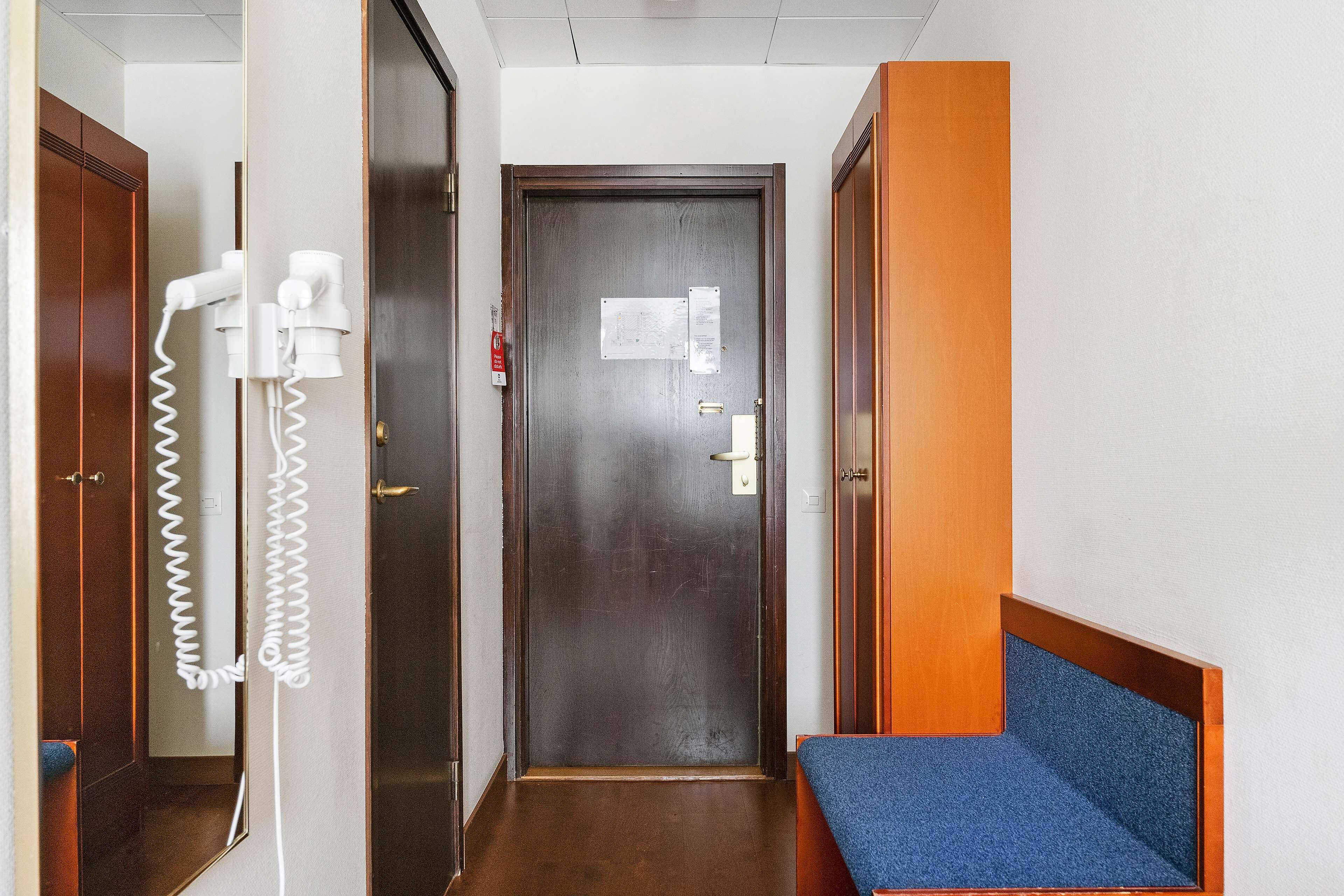 Un pasillo de hotel con una puerta de madera, un banco azul y un teléfono.